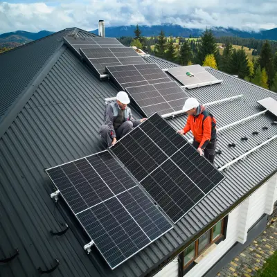 Image of 2 workers on a metal roof installing solar panels